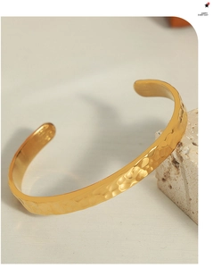 Dettaglio del bracciale rigido in acciaio al titanio dorato con finitura martellata unica