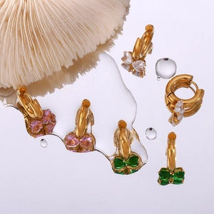 Golden bow huggie earrings with colorful heart zircons on a wet mirror surface