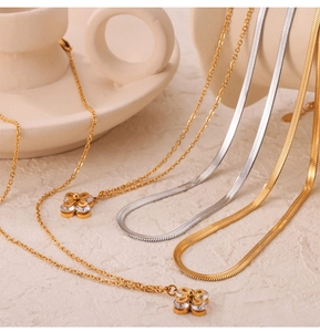 Detail of gold and silver blade chains with zircon-inlaid clover pendants on beige ceramic