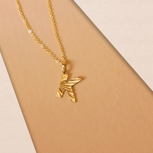 Detail of golden letter K pendant with radial texture and fine link chain necklace