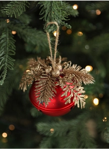Detail of red Christmas bell ornament with gold pine needles on a tree branch