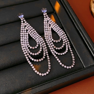 Detail of geometric silver drop earrings with purple rhinestones on a leather display