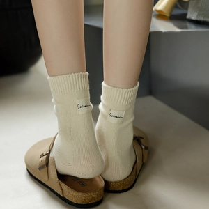 Cream knit mid-calf cotton socks with woven labels paired with brown suede clogs