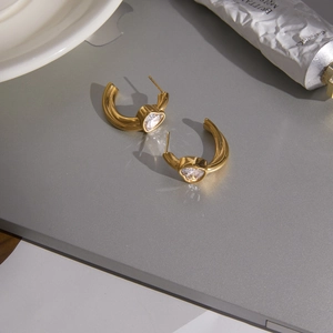 Golden C-shaped earrings with heart-shaped zircon stones on a modern grey surface