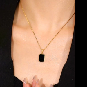Close-up of a gold titanium steel necklace with a black rectangular pendant on model