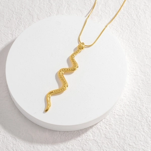 Minimalist snake pendant necklace in 18K gold plated stainless steel on white pedestal
