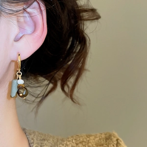 Detailed view of gold-plated puppy hoop earrings with tiger eye stone on a model ear