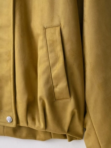 Detailed close-up of mustard yellow faux suede bomber jacket with metal snap button