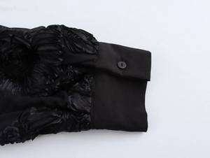 Close-up of black shirt cuff with intricate floral lace texture and matching button detail