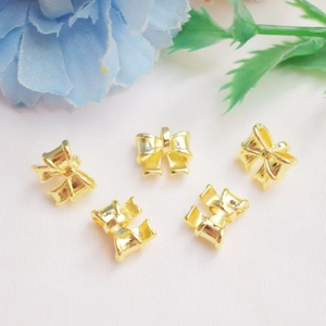 Five gold bow pendants for DIY jewelry making on soft pink fabric with floral accents