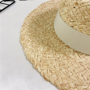 Close-up of fine hand-woven raffia straw hat texture with beige grosgrain ribbon detail