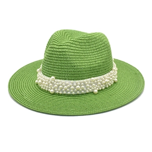 Detail of green straw fedora hat featuring white ribbon band and pearl embellishments