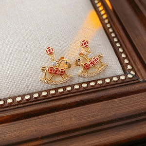 Macro view of gold rocking horse earrings with red patterns and sparkling zircon stones