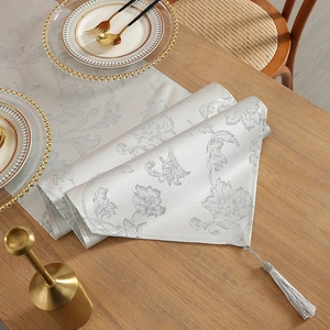 Silver grey jacquard floral table runner with tassel on wooden table with gold cutlery