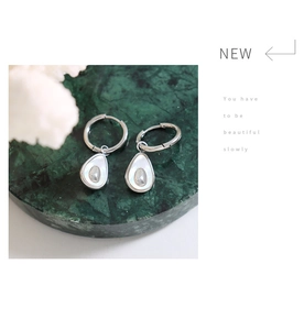 Macro detail of silver drop earrings with mother of pearl inlay and small zircon on marble