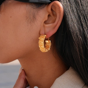 Détail d'une boucle d'oreille créole plaquée or 24 carats avec texture métal tressé