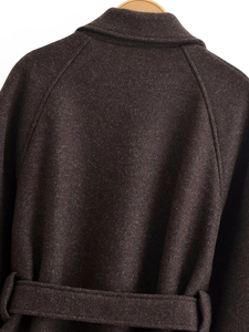Detail view of the back of a dark charcoal wool coat featuring raglan sleeves and a waist belt