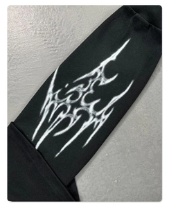 Detail eines weißen Grafikdrucks im Spray-Stil auf einem schwarzen Langarmshirt-Ärmel