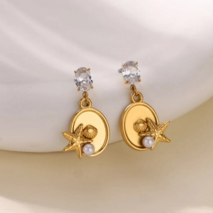 Golden ocean starfish shell earrings with pearl and zircon on white wavy background