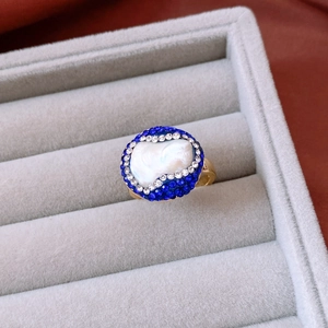 Macro view of 18k gold baroque pearl ring with blue and white pavé stones in a velvet box