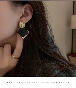 Close-up of elegant gold woven stud earrings with black square pendants on model