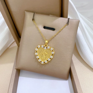 Detail of a gold heart pendant with Saint Benedict medal inlay and crystal border on a cushion