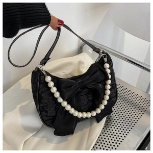 Detail of black pleated fabric bag with velvet bow and elegant pearl handle strap