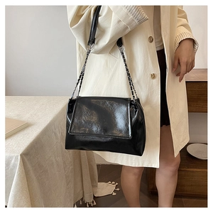 Polished black chain tote bag styled as a shoulder bag on a model in a minimalist setting