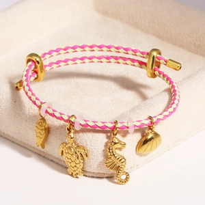 Detailed view of pink and green braided bracelet with golden ocean-themed charms in a box