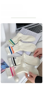 Detail of four pairs of cream ribbed crew socks with colorful stripes and smiley face patch