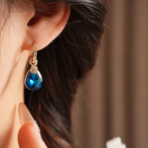 Gros plan d'une boucle d'oreille vintage dorée avec pierre goutte bleue sur un modèle