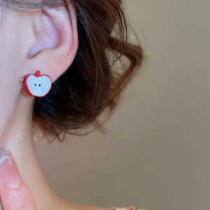 Close-up of a red enamel apple-shaped C-style stud earring worn by a model in soft light