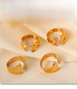 Detail of four gold PVD electroplated rings with rhinestones on beige fabric texture