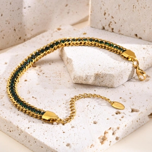 Detailed close-up of a gold chain bracelet with green square zircons on a white stone