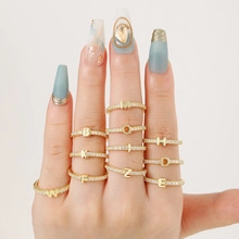 Close-up of gold plated letter rings with zircon stones worn on fingers with blue nails