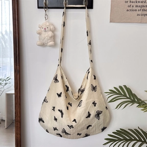 Close-up of beige canvas shoulder bag featuring black lace butterfly prints and plush lamb charm