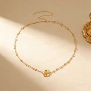 Detailopname van dubbele gouden tailleketting met een getextureerde frangipani-bloemhanger