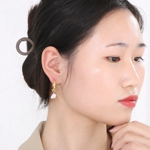 Détail d'une boucle d'oreille dorée 18 carats avec perle blanche sur un modèle