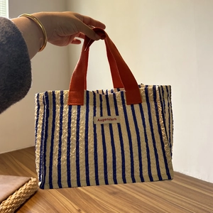 Dettaglio della borsa tote a righe blu e bianche con manici arancioni e texture seersucker