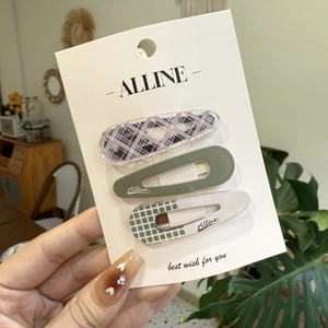 Three-piece checkered bow hair clip set in purple and green on a brand display card