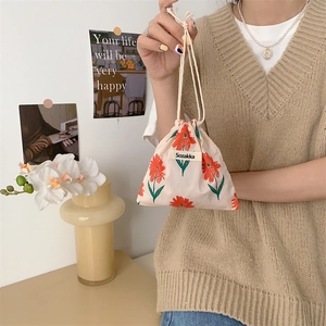 Floral drawstring bag held by hand featuring small orange flowers on beige cotton canvas