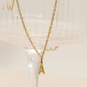 Minimalist gold stainless steel letter A pendant necklace on a striped glass edge
