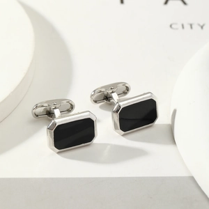 Macro detail of silver cufflinks with black enamel inlay on minimalist props
