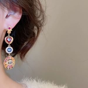 Detailed view of asymmetric heart earrings with evil eye and hand of Fatima motifs on model