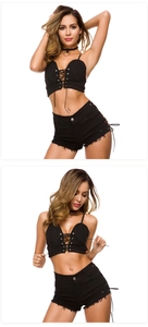 Detailansicht von schwarzem Schnür-Crop-Top und zerrissenen Jeansshorts vor weißem Hintergrund