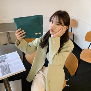 Detail of a dark green corduroy cosmetic bag held by a model in a minimalist setting