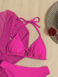 Flat lay of rose red three-piece bikini set with sheer mesh cover-up on wood background
