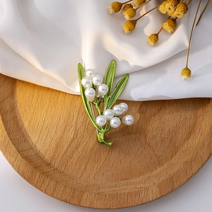Detailed view of the green leaf brooch with white pearls on a rustic wood tray