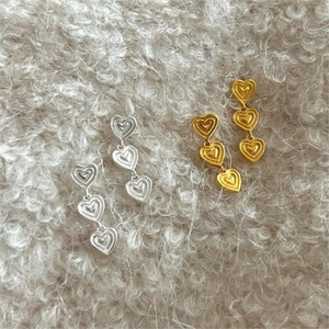 Three linked hearts drop earrings in gold and silver finish on soft plush background