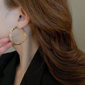 Detail of a large gold twisted geometric hoop earring worn by a model in a black blazer